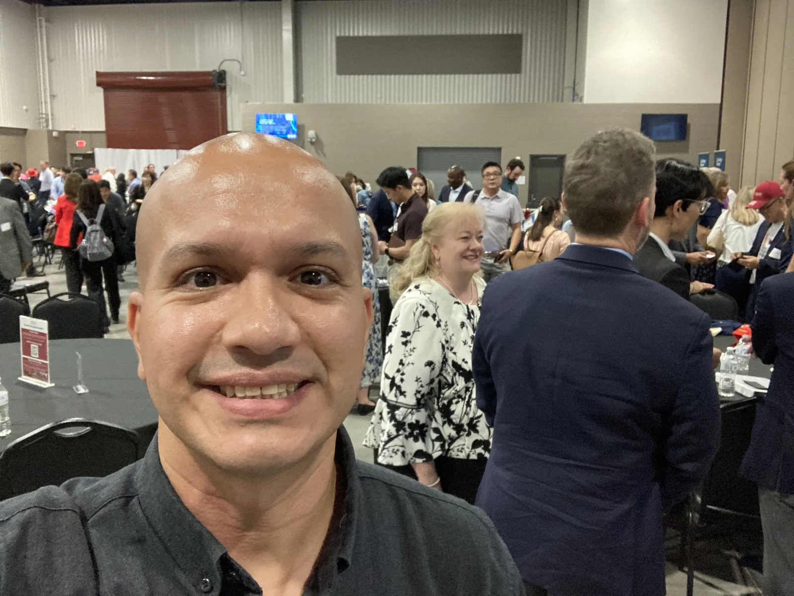 Área de networking de la Cumbre Central Texas-Corea 2026 en el Wilco Expo Center. Decenas de asistentes conversan de pie entre mesas redondas en un salón amplio antes del inicio del programa.