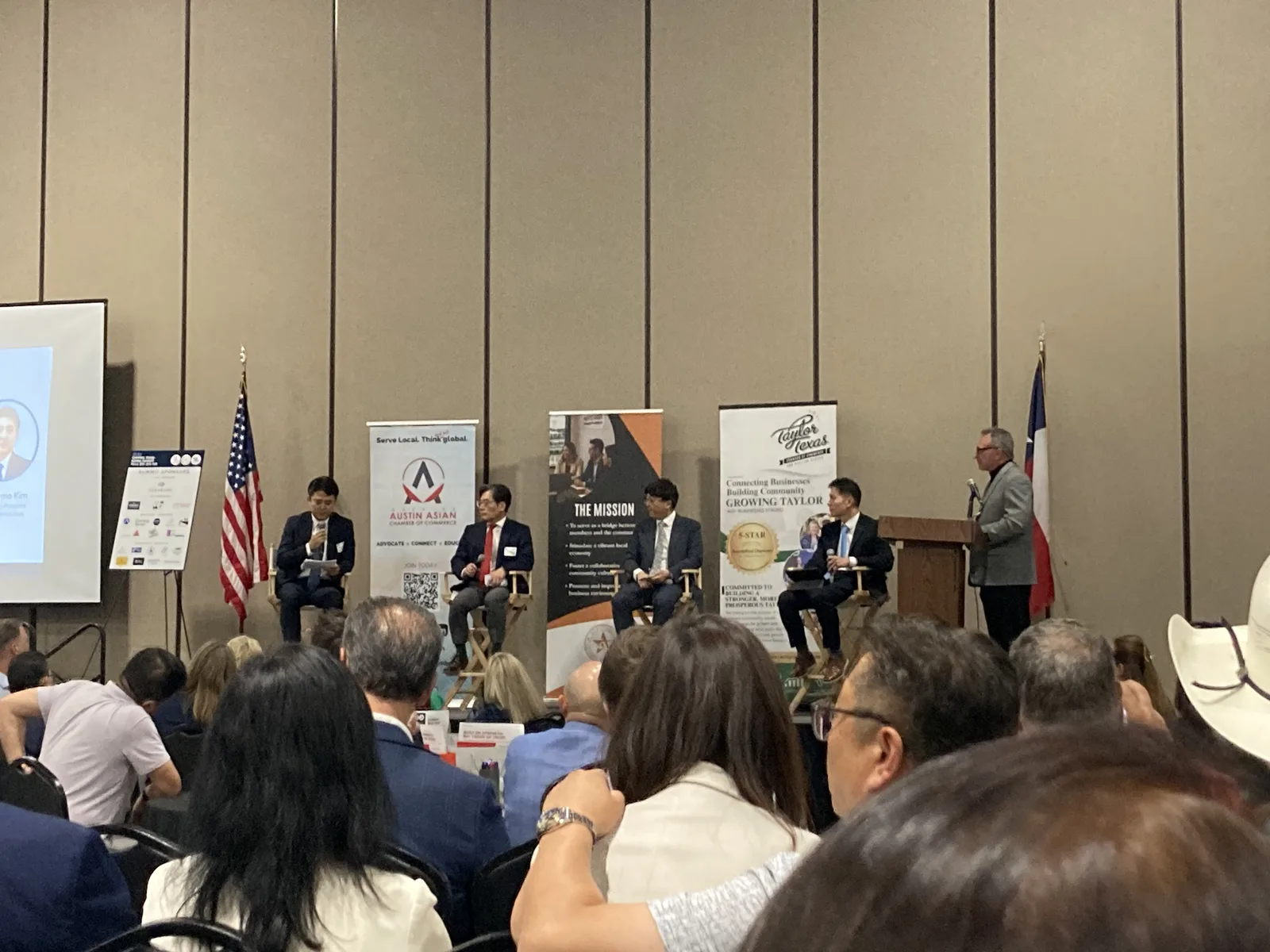 Panel de discusión de la Cumbre Central Texas-Corea 2026 en el Wilco Expo Center de Taylor, Texas. Cuatro panelistas sentados en el escenario frente a una audiencia llena, con banderas de Estados Unidos y Texas y los pendones de la Greater Austin Asian Chamber of Commerce y la Greater Taylor Chamber of Commerce al fondo.