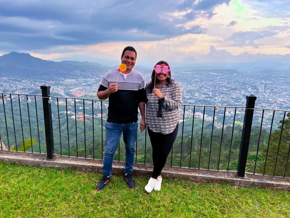 Two Andes Development team members smiling and using festive props during the 12th anniversary corporate gathering. In the background, a stunning panoramic view of the city and mountains at sunset.