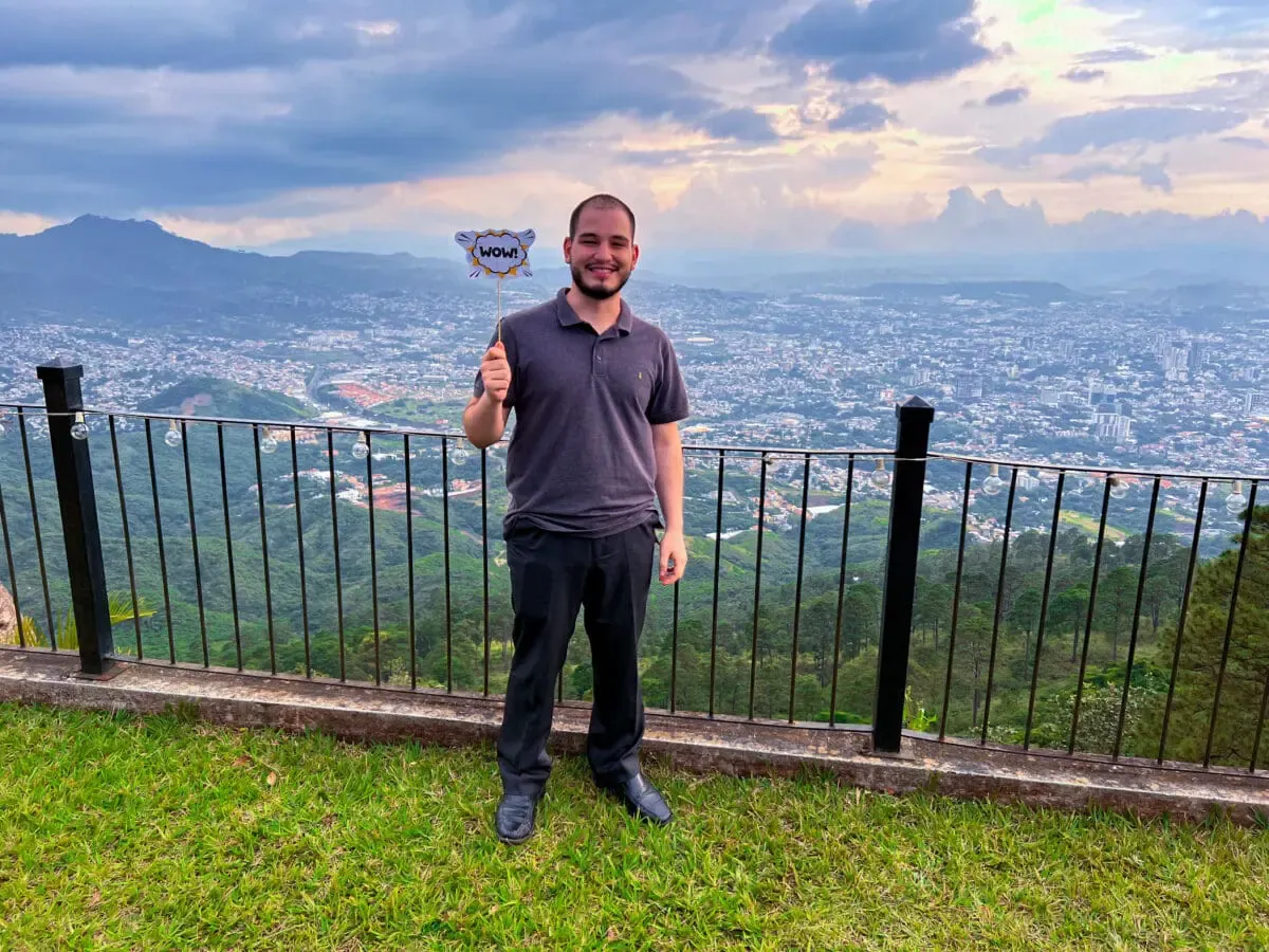 Andes Development team member smiling with a 'WOW!' sign during the corporate celebration of the agency's 12 years, with a beautiful sunset and the city in the background.