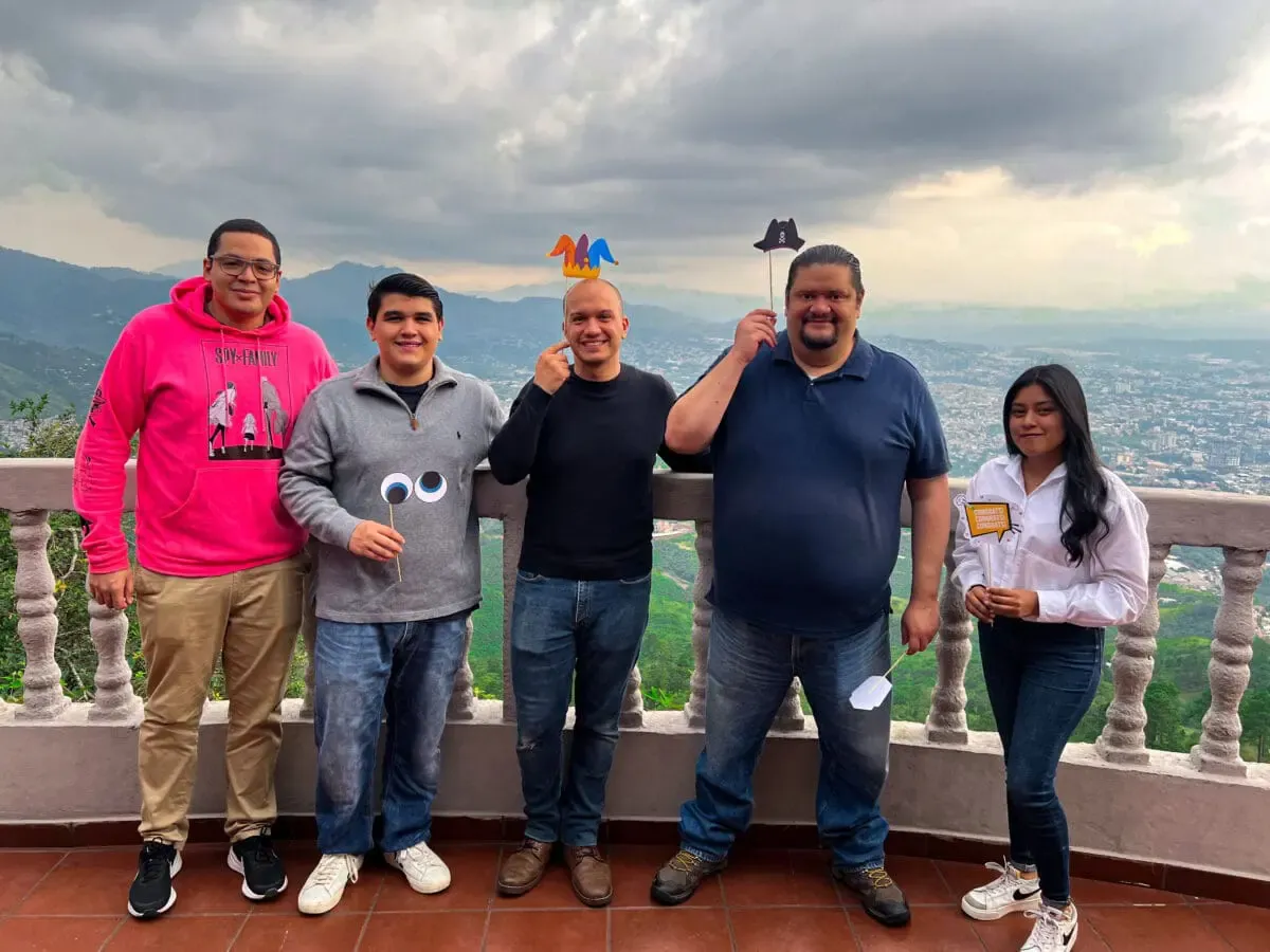Group of five Andes Development team members sharing a fun moment with playful prop signs during the celebration of the agency's 12-year journey, with an urban sunset landscape in the background.
