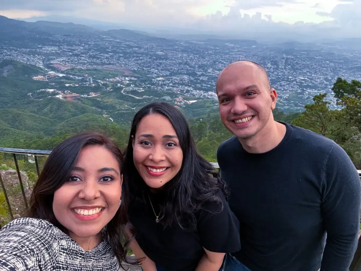 Selfie of three Andes Development team members enjoying the corporate gathering for the 12th anniversary. The team members pose smiling outdoors with a beautiful urban and natural landscape behind them.