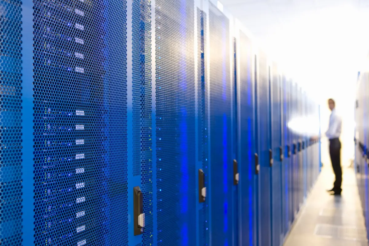 Fila de gabinetes de servidores de red iluminados en azul brillante dentro de un centro de datos corporativo. Ilustra las opciones de infraestructura tecnológica, desde arquitecturas monolíticas hasta microservicios, y la gestión eficiente en la nube mediante partners institucionales como AWS.