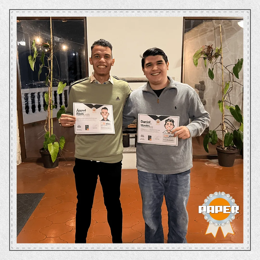 Ángel Ríos y Daniel Morales posando sonrientes con sus diplomas del Premio Paper durante la celebración del 12º aniversario de Andes Development. Este premio reconoce su talento, crecimiento y dedicación durante sus primeros dos años en la agencia.